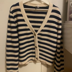 Randig kofta med v-ringning och knappar - Snygg randig kofta i mörkblått och beige med v-ringad hals och tre knappar framtill. Stickad struktur och långa ärmar ger en chill och klassisk vibe. Perfekt att slänga över en t-shirt för extra stilpoäng.