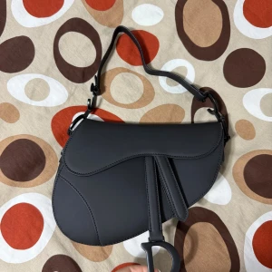 Svart Saddle handväska  - Supersnygg svart Saddle handväska i skinn. Liten skada se bild 3. Box ingår och pris kan diskuteras vid snabb affär