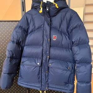 Blå Fjällräven Expedition dunjacka S - Säljer en blå Fjällräven Expedition Down Jacket från 1974-serien, dammodell i storlek S. Jackan har huva med gula snören, två stora fickor med knappar, dragkedja och tryckknappar framtill samt ikonisk Fjällräven-logga på bröstet. Perfekt för kalla vinterdagar. Köptes dec 2024 och använd max 5ggr.  Säljes pga av att den känns för stor. 
