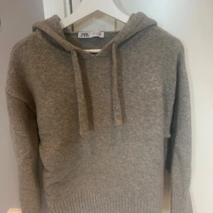 Grå stickad hoodie från Zara med huva - Mysig grå hoodie från Zara i storlek M. Tröjan har huva med snörning och ribbad nederkant. Materialet är stickat och känns mjukt mot huden, perfekt för kyliga dagar. Enkel och stilren design som funkar till jeans eller mjukisbyxor.