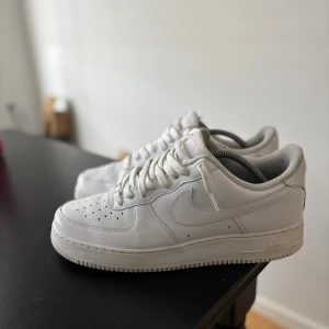 Nike Air Force 1 vita sneakers - Fräscha Nike Air Force 1 sneakers i helvitt skinn med klassisk låg siluett. Snygga perforeringar på tån för extra ventilation och ikonisk swoosh på sidan. Platt sula och snörning för en clean look som alltid funkar.