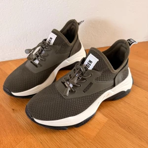 Steve Madden Match Olivgröna sneakers - Snygga olivgröna sneakers från Steve Madden med stickad ovandel och vita, chunky sulor. Skorna har snörning med elastiska snören och svarta detaljer på sulan. Praktiska dragflikar med logga bak och framtill. Perfekt för dig som gillar sportig och modern stil. Storleken är 39 och endast använda 1 gång. Nypris 1 149kr mitt pris 650kr. 