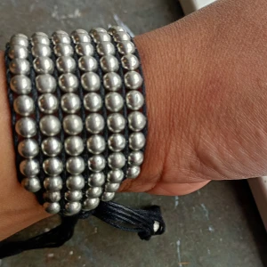 Svart och silver pärlarmband - Säljer ett brett armband med flera rader silverfärgade pärlor på svart snöre. Armbandet har justerbar knytning och en cool, chunky look som sticker ut. Perfekt för dig som gillar att addera lite edge till din stil.