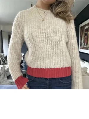 Beige stickad tröja med rosa detaljer - Mysig beige stickad tröja med ribbstickade muddar och nederkant i rosa.