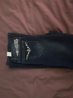 Mörkblå jeans med nitar och brodyr - Snygga mörkblå jeans med raka ben, dekorerade bakfickor med silvriga nitar och broderade vingar. Jeansen har kontrastsömmar och coola detaljer som ger en unik look. Perfekta för dig som vill sticka ut lite extra. Aldrig andvända 💕