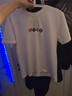 Vit HUGO t-shirt med design - Vit t-shirt från HUGO med tryck av spelkort och texten 'Full House' på ryggen samt små symboler och HUGO-logga framtill. Klassisk passform med rund hals och korta ärmar. Perfekt för dig som gillar unika prints och streetstyle.