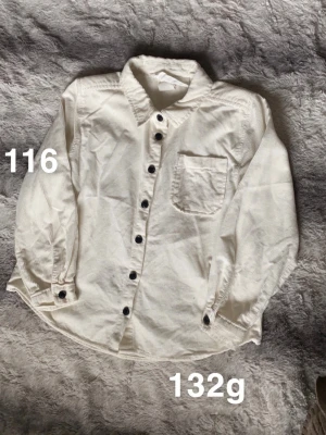 Vit manchester skjorta med knappar - Vit skjorta i mjuk manchester med svarta knappar framtill och en bröstficka. Klassisk krage och långärmad modell. Perfekt för en avslappnad men ändå stilren look.