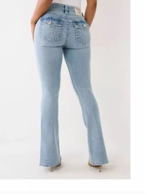 Ljusblå bootcut jeans True Religion - Säljer ett par ljusblå bootcut jeans från True Religion med ikoniska bakfickor och tydliga kontrastsömmar. Jeansen har klassisk femficksdesign, silverfärgade knappar och patch med logga bak i midjan. Tillverkade i denim med snygg tvätt.
