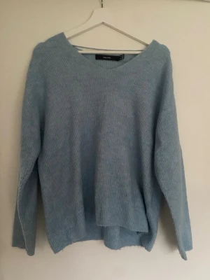 Ljusblå stickad tröja Vero Moda - Mysig ljusblå stickad tröja från Vero Moda med v-ringad hals och avslappnad passform. Tröjan har långa ärmar och är ribbstickad i ett mjukt material, perfekt för kyliga dagar. Enkel och stilren design som passar till det mesta.