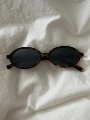 Ovala solglasögon i brunmelerad plast - Snygga ovala solglasögon med brunmelerad båge och mörka glas. Bågarna har en retroinspirerad look och är tillverkade i plast. Perfekta för att lyfta din stil under soliga dagar.