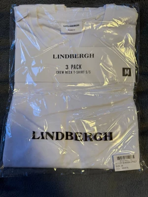 Vit t-shirt 3-pack från Lindbergh - Säljer ett 3-pack vita t-shirts från Lindbergh med klassisk rund halsringning och korta ärmar. T-shirtsen har en clean look med diskret Lindbergh-logga framtill. Perfekt basplagg till garderoben.