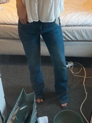 Mörkblå raka jeans - Säljer ett par mörkblå jeans med rak passform och klassisk femficksdesign. Jeansen har normal midja och är tillverkade i ett denimtyg som ger en tidlös look. Perfekta att matcha med både skjorta och t-shirt.