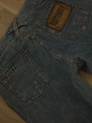 Blåa jeans från Dolce&Gabbana - Säljer ett par blåa jeans från dolce&Gabbana med slitna detaljer och raka ben. Jeansen har flera fickor fram och bak samt en snygg läderpatch med logga bak. Materialet är klassisk denim i bomull. Perfekta för en avslappnad och trendig look.