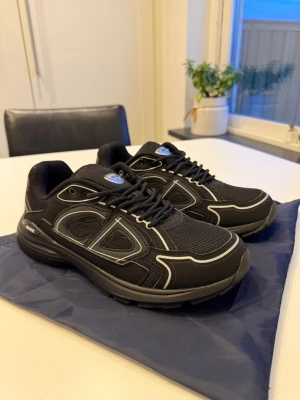 Svarta Dior B30 sneakers/skor - Snygga svarta Dior B30 sneakers med reflekterande detaljer och meshpaneler. Skorna har en sportig design med tydlig Dior-logga på sidan och plös, samt svarta snören och robust sula. Perfekta för dig som gillar exklusiva och trendiga sneakers.        📦Fraktas samma dag📦  ⭐️Helt ny samt oanvänd⭐️  Har du frågor eller funderingar så hör gärna av dig🤗 Dustbag samt box osv följs med vid köp⚡️