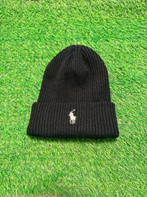 Svart ribbstickad mössa från Polo Ralph Lauren - Svart ribbstickad mössa från Polo Ralph Lauren med klassisk uppvikt kant och den ikoniska vita polospelaren broderad framtill. Perfekt accessoar för kyliga dagar och enkel att matcha med olika stilar.