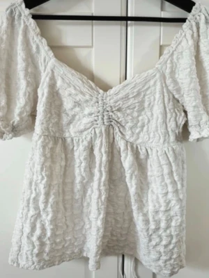 Vit blus / topp med puffärmar - Söt vit blus/top med puffärmar och fin detaljering i materialet, även knytning bak i ryggen. Köpt här på vinted (lånade bilder från förra säljaren), men blusen är först från ginatricot. Den har inte kommit till användning tyvärr. Väldigt bra skick.  Perfekt nu inför våren och sommaren och passar bra till både jeans och kostymbyxor. 