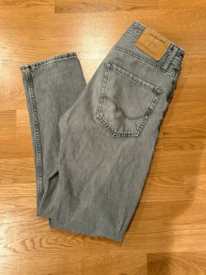 Grå jeans från Jack & Jones - Ett par klassiska grå jeans från Jack & Jones i rak modell. Jeansen har fem fickor, normalhög midja och är tillverkade i denim. Perfekta för dig som gillar en stilren och enkel look.