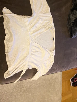 Vit omlottopp från Gina Tricot - Snygg vit omlottopp från Gina Tricot i mjukt och lätt bomullsmaterial. Toppen har långa ärmar och knytband i midjan för en feminin siluett. Perfekt att styla med jeans eller kjol för en trendig look.