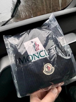 Moncler Mössa  - Snygg svart ribbstickad mössa från Moncler med klassisk Moncler-logga framtill. Mössan har uppvikt kant och är tillverkad i ett mjukt och värmande material, perfekt för kyliga dagar. En stilren accessoar som lyfter din outfit. Tag och äkthetsmärke finns kvar. 