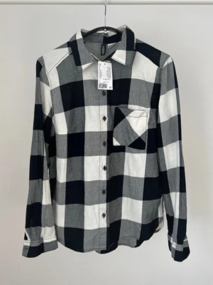 Rutig skjorta från H&M i svart och vit - Säljer en ny rutig skjorta från H&M Divided i svart, grått och vitt. Skjortan har klassisk krage, bröstficka och knappar framtill 🖤