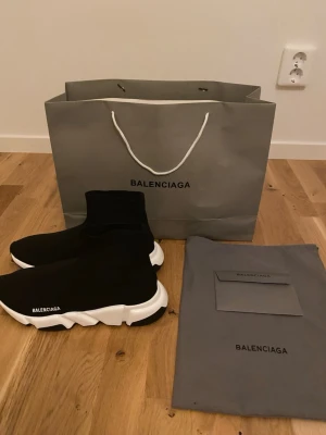 B Speed Trainer svarta sneakers - Svarta B Speed Trainer sneakers med vit chunky sula och stickad strumpliknande ovandel. Minimalistisk design med B-logga på sidan. Skorna är lätta och flexibla, perfekta för en trendig streetwear-look.