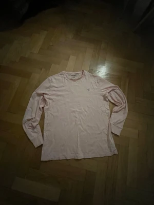 Longsleeve t-shirt från Polo Ralph Lauren - Ljusrosa långärmad tröja från Polo Ralph Lauren med klassisk rund halsringning och broderad logga på bröstet. Tillverkad i mjuk bomull, perfekt för en avslappnad och stilren look. Den är lite urtvättad men fortfarande väldigt fint skick utan några fläckar eller liknande.