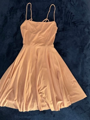 Ljusrosa kort klänning - Söt ljusrosa kortklänning med smala axelband. Storlek S. Klänningen har en enkel, stilren design och tunna band som korsas i ryggen. Perfekt för sommarens varma dagar.