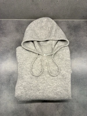Kashmir tröja  - En stilren ljusgrå hoodie med huva och dragsnören. Tillverkad i en mjuk och skön ullmix som känns lyxig mot huden. Klassisk passform med ribbade muddar vid ärmslut och nederkant. Perfekt för dig som gillar en clean och enkel look.