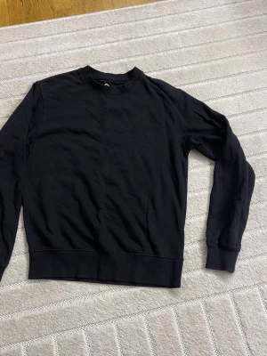 Svart basic sweatshirt - En enkel svart sweatshirt med rund hals och ribbade muddar vid ärmslut och nederkant. Perfekt oversized fit för en avslappnad look. Tillverkad i mjukt bomullsmaterial som känns skönt mot huden.