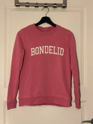 Rosa sweatshirt från Bondelid - Rosa sweatshirt från Bondelid med vit text framtill. Tröjan har rund halsringning, långa ärmar och ribbade muddar vid ärmslut och nederkant. Perfekt för en avslappnad och stilren look.