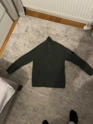 Mörkgrön stickad tröja C.P. Company - Säljer en mörkgrön stickad tröja från C.P. Company med hög krage och knappar framtill. Tröjan har en ficka på ärmen med den klassiska svarta linsen. Grovstickad och riktigt snygg till hösten och vintern. Strl S köpt på BOYES2men i Falkenberg 