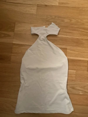 Vit axelbandslös topp - Säljer en stilren vit axelbandslös topp med unik form och knappdetalj vid halsen. Toppen har en smal passform och är tillverkad i ett mjukt, stretchigt material som känns bekvämt mot huden. Perfekt att styla till olika outfits.