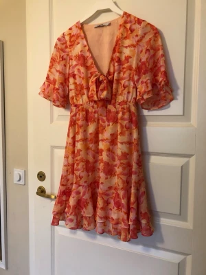 Blommig kortklänning med volang - Jättefin klänning i blommigt korallmönster från NA-KD i storlek 32. Passar även 158-164. Inga anmärkningar, nyskick. Fodrad, ej genomskinlig.