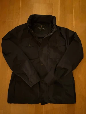 Blå field jacket från Bondelid - Snygg blå vindjacka från Bondelid med hög krage och tryckknappar framtill. Skick 9/10 inte använd mycket alls. Passar dig mellan 180-185 nog. Nypris ligger på 1800kr. Pris ej hugget i sten!