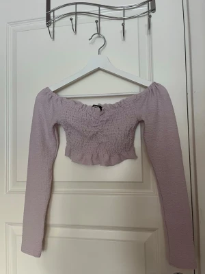 Ljuslila off shoulder topp - Trendig ljuslila off shoulder topp från Bik Bok med smockad midja och volangkant. Långärmad modell i stretchigt tyg som sitter snyggt och bekvämt. 