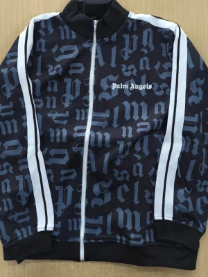 Palm Angels ziptröja med tryck - Snygg svart ziptröja från Palm Angels med vit logga på bröstet och gotiskt mönster över hela tröjan. Tröjan har vita ränder längs ärmarna, ribbade muddar och hög krage. Perfekt för dig som gillar streetwear och vill sticka ut.