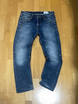 Blå raka jeans från Emilio - Säljer ett par klassiska blå jeans från Emilio med rak passform och snyggt slitna detaljer. Jeansen har fem fickor, knappgylf och är gjorda i kraftig denim. Perfekta för en avslappnad och trendig look.