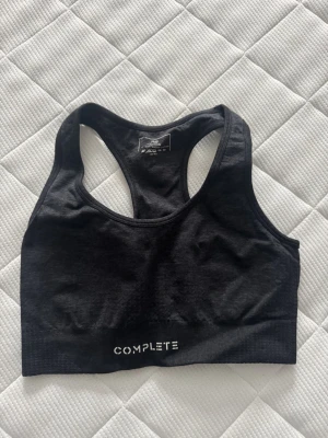 Svart sport-bh från Complete - Sport-bh i svart från Complete med brottarrygg. Tillverkad i en mjuk och stretchig blandning av polyester och spandex. Perfekt för träning eller en aktiv vardag. Diskret logga framtill.