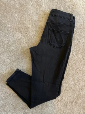 Svarta skinny jeans med hög midja - Snygga svarta skinny jeans med hög midja och klassiska fem fickor. Jeansen har en smal passform och är tillverkade i stretchigt material för extra komfort. Perfekta för dig som gillar en stilren och enkel look.