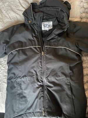 Svart dunjacka från CRW  - Svart dunjacka från CRW med avtagbar huva och dragkedja framtill. Jackan har reflex detaljer längs bröstet. Smidig att rida med och varm, har använts men det syns ej. Är i storlek 146-152.💗