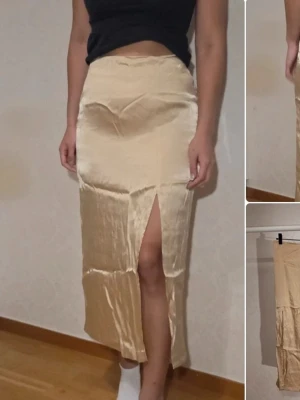 Champagnefärgad satinkjol & Other Stories - Snygg långkjol i champagnefärgad satin från & Other Stories. Kjolen har en rak passform med hög midja och en slits framtill som ger en trendig look. Perfekt att styla med crop top eller stickad tröja för en cool vibe.
