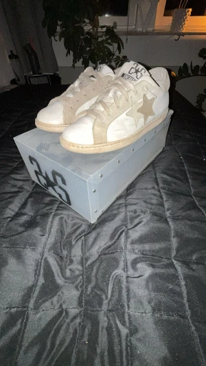 Vit-beige sneakers från 2STARE - Säljer ett par snygga sneakers från 2STARE i vit och beige färg. Skorna har en rund tå, platt sula och är dekorerade med två stjärnor på sidan. Ovandelen är i skinn och mocka, med snörning framtill. Perfekt för dig som gillar stilrena detaljer och neutrala toner.