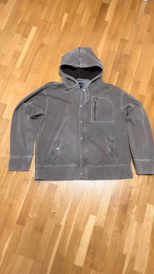 Beige olivgrön teddyjacka med huva från GAP - Säljer en beige olivgrön teddyjacka från GAP med huva och snörning. Jackan har mjukt teddyfoder, tryckknappar och dragkedja framtill, samt fickor med knappstängning och en bröstficka med dragkedja. Perfekt för kalla dagar och chill stil.