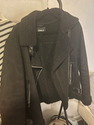 Svart teddyjacka från ONLY, S - Hejjj!! Säljer en svart teddyjacka från ONLY i storlek S. Har använt den en vinter men den är i väldigt fint skick. Säljer den bara då jag växt ifrån den annars hade jag behållt den. Jackan har mjukt teddyfoder, bred krage, två fickor med dragkedja och snygga bältesdetaljer vid kragen och nederkanten. Perfekt för kalla dagar med sin mysiga och stilrena look. Det hänger lite trådar runt halsen men annars är jackan som ny. 