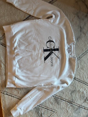 Vit sweatshirt från Calvin Klein Jeans - Jag inbjuder dig att köpa en tröja av mycket god kvalitet från Calvin Klein. Tröjan är 2 år gammal och i mycket gott skick. Den användes av en flicka. Storlek M/38.  Calvin Klein Jeans Tröjan har rund hals, långa ärmar och ribbade muddar vid ärmslut och nederkant. Perfekt för dig som gillar stilrena och klassiska plagg med tydlig logga. Välkommen!