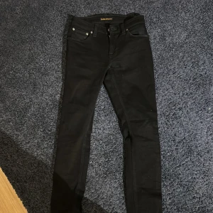 Svarta jeans från Nudie Jeans - Svarta jeans från Nudie Jeans med klassisk femficksdesign och snygga detaljer på bakfickorna. Jeansen är tillverkade i stretchigt bomullsmaterial för extra komfort. Perfekt för dig som gillar en stilren och modern look. Modellen S4 om du vill se mer bilder. Priset kan diskuteras! Fråga om mer bilder ifall det behövs.