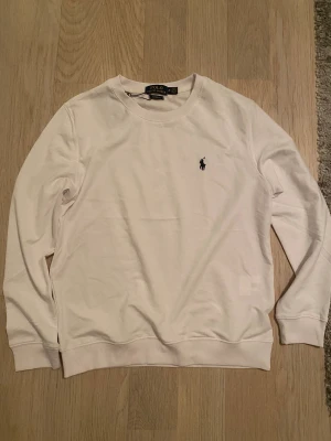 Vit långärmad tröja från Polo Ralph Lauren - Vit långärmad tröja från Polo Ralph Lauren i mjuk bomull. Klassisk rund hals och ikonisk broderad logga på bröstet. Perfekt för dig som gillar stilrena och enkla plagg med premiumkänsla. Passar dig som vill ha en clean look.
