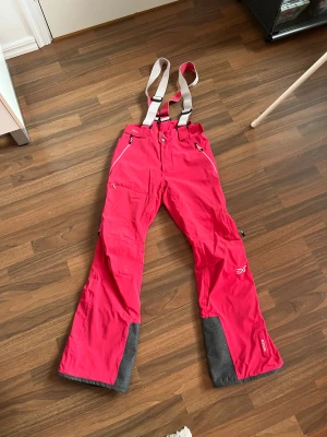 Termobyxor/skidbyxor från Everest  - Everest i storlek M i rosa färg. Byxorna har justerbara hängslen och flera fickor med dragkedjor. Materialet är anpassat för utomhusbruk med förstärkningar vid knä och nederdel. Produkten är utrustad med RECCO-reflektor för ökad säkerhet vid aktiviteter i snö.  Avtagbara hängslen och kardborre i midjan för enkel justering. Väldigt fint skick!