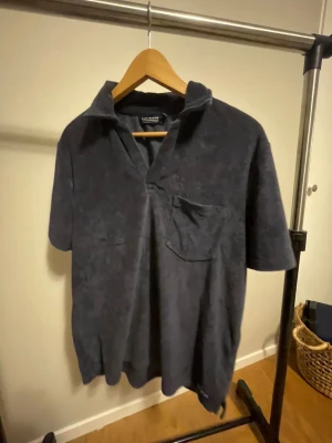 Mörkblå frotté pikétröja  - Snygg mörkblå henley-skjorta från Warp i mjuk frotté. Skjortan har korta ärmar, öppen krage och en bröstficka som ger en chill vibe. Perfekt för dig som gillar bekväma och stilrena plagg med lite extra känsla.