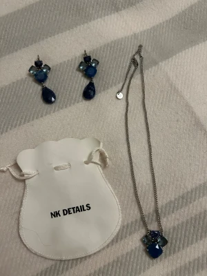  Nya Blått smyckeset från Deberg Kern  - Snyggt smyckeset med örhängen och halsband från Deberg Kern . Båda har silverfärgad metall och blå stenar i olika former, med droppformad detalj på örhängena och matchande hängsmycke på halsbandet. Perfekt för dig som gillar färgstarka accessoarer.
